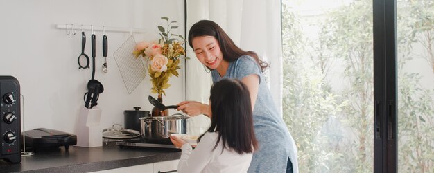 若いアジアの日本人ママと娘が自宅で料理します。朝は家のモダンなキッチンで朝食の食事のためにパスタとスパゲッティを一緒に作る幸せなライフスタイルの女性。