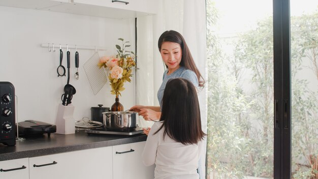 若いアジアの日本人ママと娘が自宅で料理します。朝は家のモダンなキッチンで朝食の食事のためにパスタとスパゲッティを一緒に作る幸せなライフスタイルの女性。