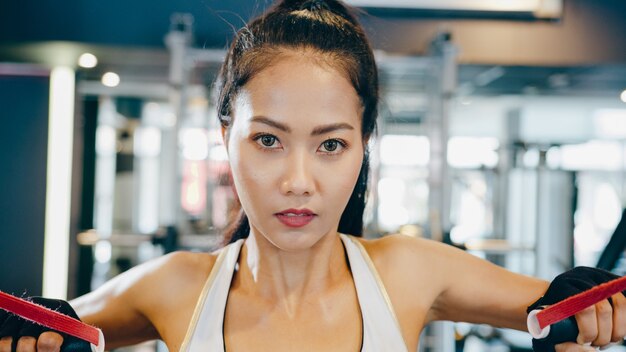 Young asian lady doing exercise-machine Cable Crossover in fitness class