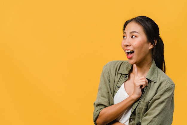 La giovane donna asiatica si sente felice con l'espressione positiva, gioiosa sorpresa funky, vestita con un panno casual isolato sul muro giallo. la donna felice adorabile felice si rallegra del successo. espressione facciale.