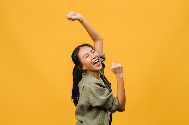 Young Asian lady with positive expression, joyful and exciting, dressed in casual cloth over yellow wall with empty space. Happy adorable glad woman rejoices success. Facial expression concept.