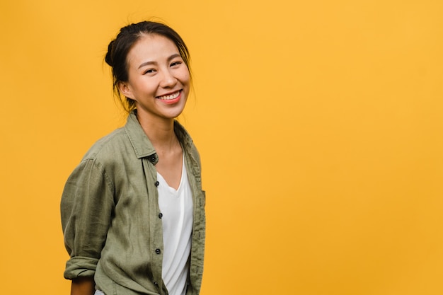 Foto gratuita giovane signora asiatica con un'espressione positiva, sorride ampiamente, vestita con abiti casual sul muro giallo. la donna felice adorabile felice si rallegra del successo. concetto di espressione facciale.