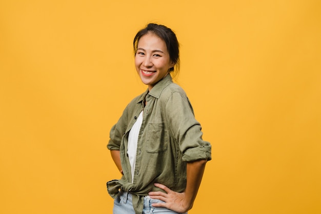 무료 사진 긍정적인 표정을 지닌 젊은 아시아 여성은 노란 벽 위에 평상복을 입고 활짝 웃고 있습니다. 행복하고 사랑스러운 기쁜 여자는 성공을 기뻐합니다. 표정 개념입니다.