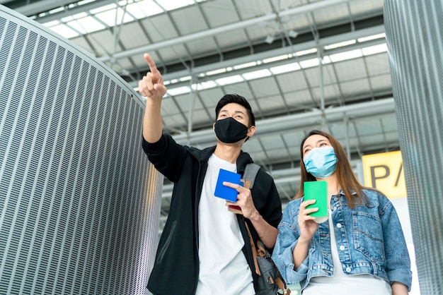 Free photo young asian male and female couple tourists drag luggages walking through the hallway after arrival two asian people traveller wearing facial face mask virus protection safety travel ideas concept