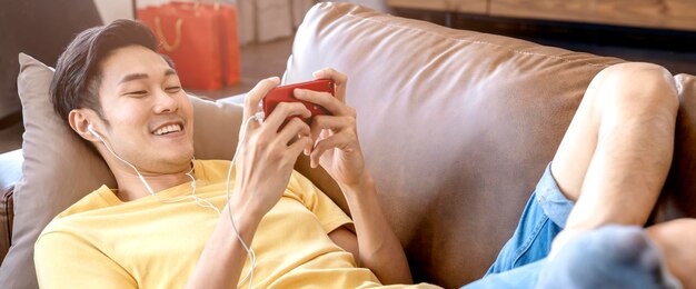 Young asian male hand playing smartphone gaming online casual and leisure exiting and jpyful laydown on sofa on weekend at home quarantine activity ideas concept