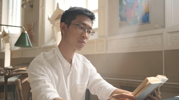 Young asian male student intently reading book in library of university Attractive guy preparing for exams in college campus