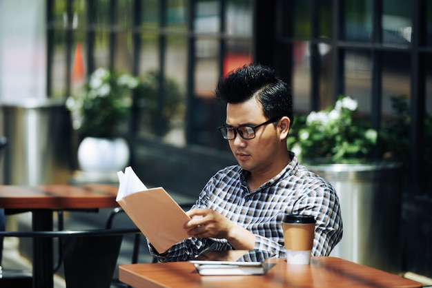 屋外カフェに座って本を読んでメガネの若いアジア人