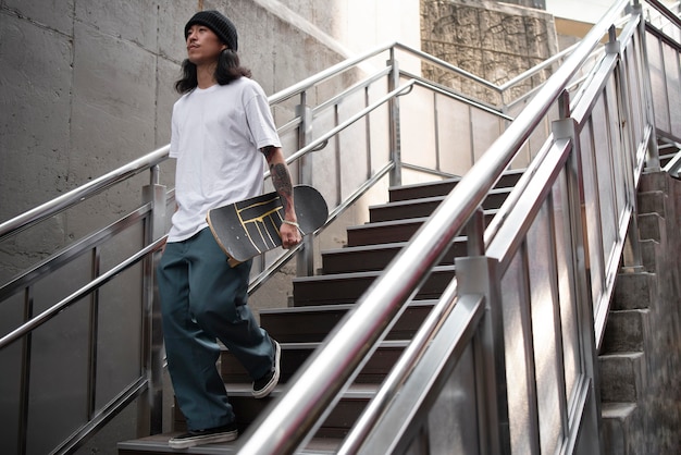 Free photo young asian man holding his skateboard