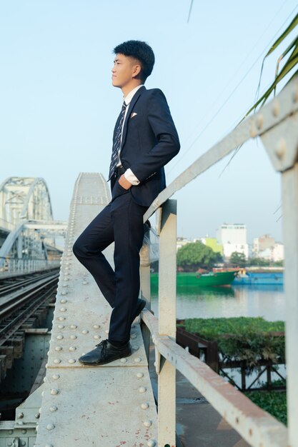 Young Asian man leaning on a bridge looking away