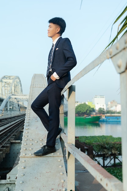Молодой азиатский мужчина, опираясь на мост, глядя в сторону