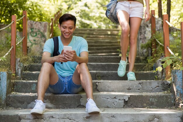 Young asian man outdoors sitting on ladder chatting by phone.