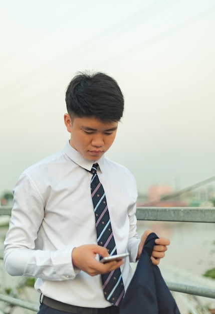 Free photo young asian man in a suit sending message on his hone