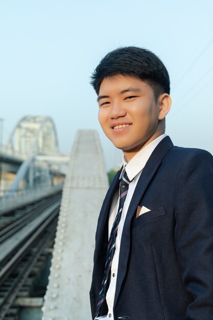 Young Asian man in a suit smiling and standing on a bridge