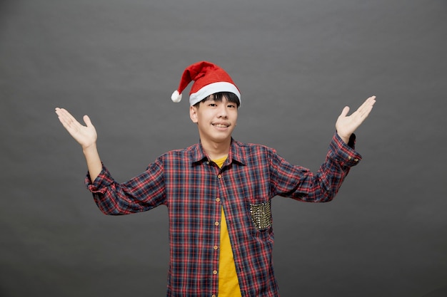 スタジオショットでクリスマスの帽子をかぶって、灰色の背景で隔離の若いアジア人男性