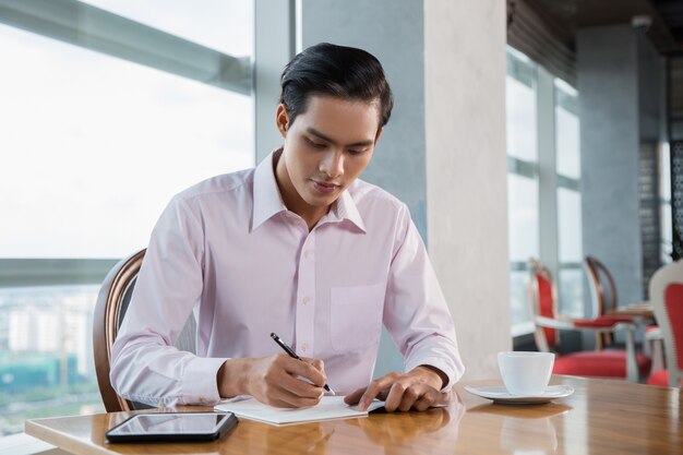 Young Asian Man Writing in Cafe