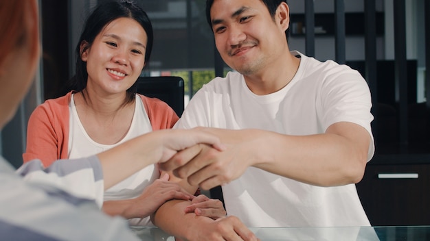 Young Asian Pregnant couple sign contract documents at home, Japanese family consulting with real estate financial advisor, Buying new house and handshaking with broker in living room in the morning.