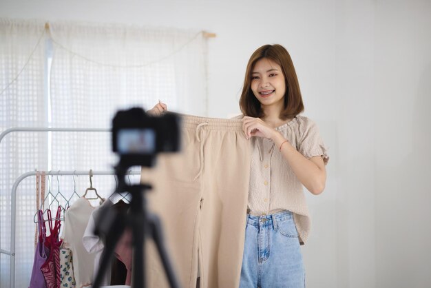 젊은 아시아 판매자 소녀는 여성 옷을 보여주고 소셜 미디어 개념이 있는 가정 온라인 시장에서 온라인으로 비디오 라이브 스트리밍을 만듭니다.