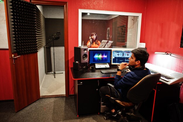 Young asian singer with microphone recording song in record music studio with sound producer