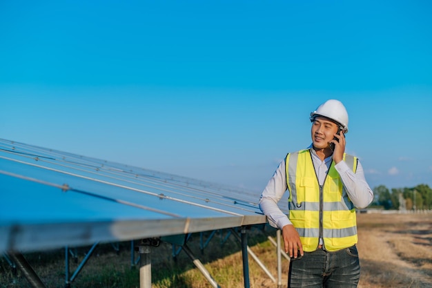 Free photo young asian technician man standing and talking on smartphone between long rows of photovoltaic solar panels copy space