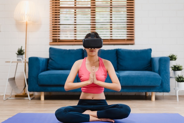 Giovane donna asiatica dell'adolescente che utilizza il simulatore di realtà virtuale mentre praticando yoga in salone