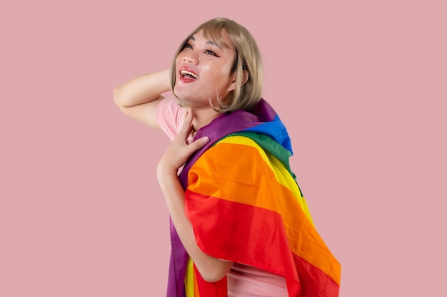 Young Asian transgender LGBT with Rainbow flag isolated over pink color background Gender expression pride and equality concept