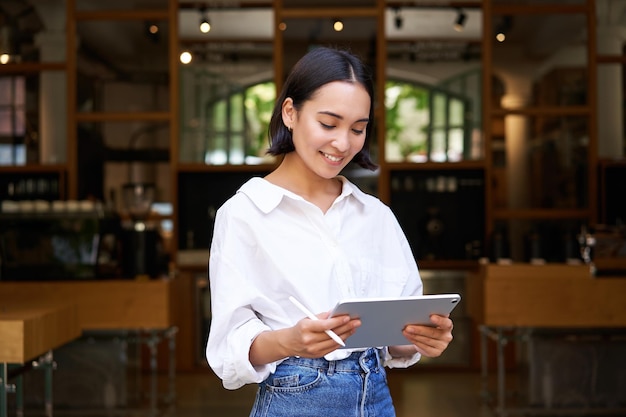 Бесплатное фото Молодой азиатский менеджер кафе официантки, работающий с планшетом и графическим планшетом