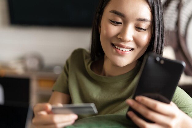 집에서 휴대 전화와 신용 카드 쇼핑을 사용하여 온라인 상점에서 구매하는 젊은 아시아 여성