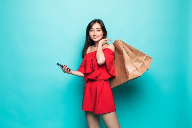 녹색 벽에 고립 된 전화로 쇼핑 가방 및 문자 메시지를 들고 젊은 아시아 여성