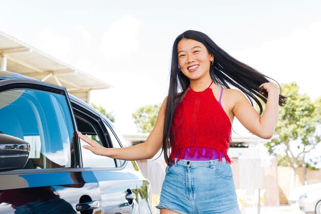 Young Asian woman closing car door and touching hair