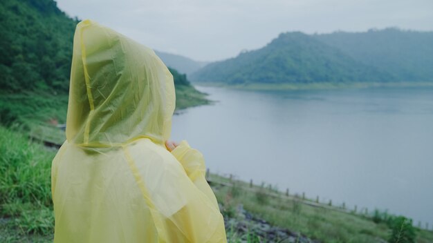 Young Asian woman feeling happy playing rain while wearing raincoat standing near lake