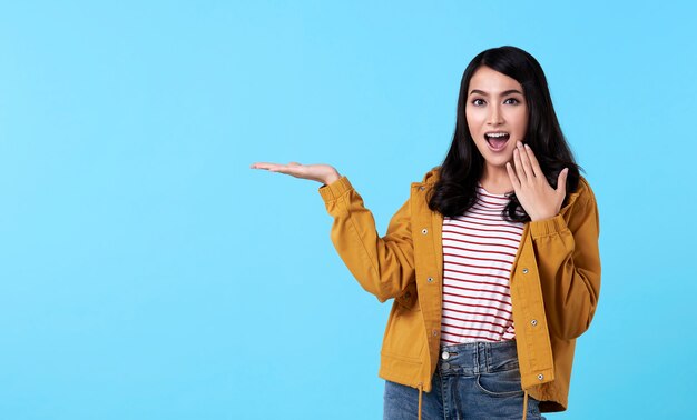 Young asian woman gesture presenting an idea with hand open to copy space isolated on blue background.