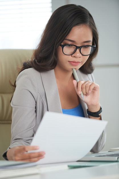 사무실에서 책상에 앉아 문서를 공부하는 안경에 젊은 아시아 여자