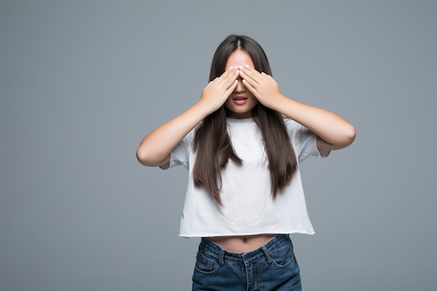 Young asian woman hides her face, studio photo on gray background. social phobia problem concept. Girl covers face with hands feeling fear emotion.