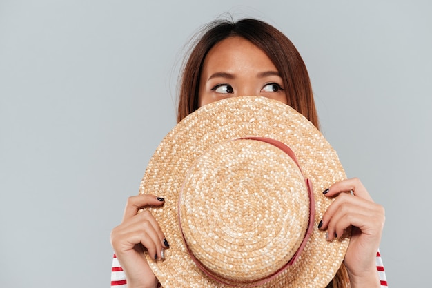 Young asian woman hiding behind a hat and looking away