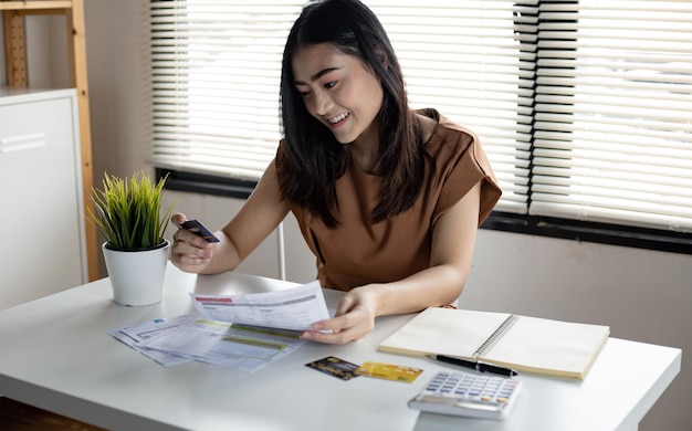 Young asian woman holding credit card and bill with smile at work table in home. women smile happily after no debt. not worried about the problems caused by credit card debt.