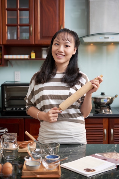 麺棒を押しながら自宅のキッチンでポーズをとって若いアジア女性