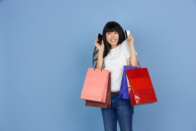 Young asian woman holding shopping bags on blue