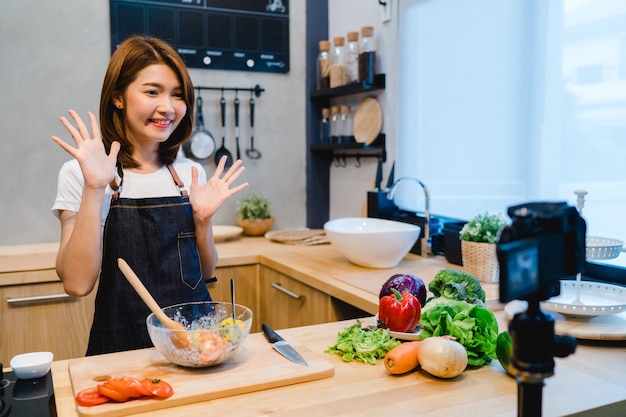 Young asian woman in kitchen recording video on camera