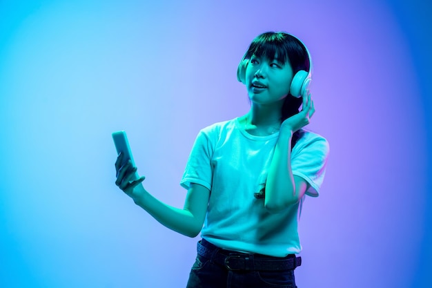 Young asian woman's portrait on gradient blue-purple in neon light