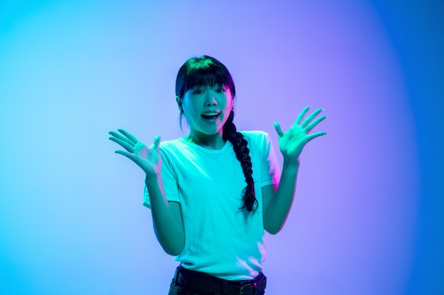 Young asian woman's portrait on gradient blue-purple studio background in neon light. Concept of youth, human emotions, facial expression, sales, ad. Beautiful brunette model.