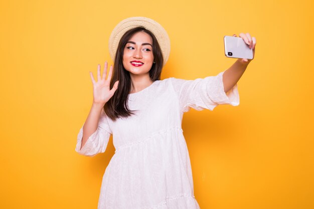 Молодая азиатская селфи женщины при мобильный телефон изолированный на желтой стене