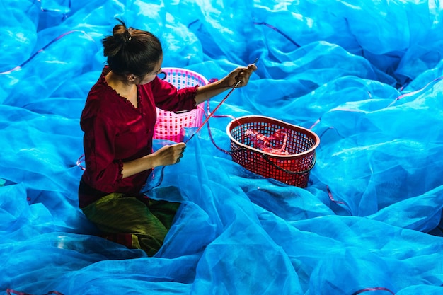 Молодая азиатка шьет рыболовную сеть в рыбацкой деревне