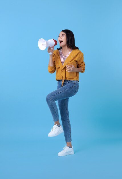 Young Asian woman shouting into megaphone making announcement in on blue.