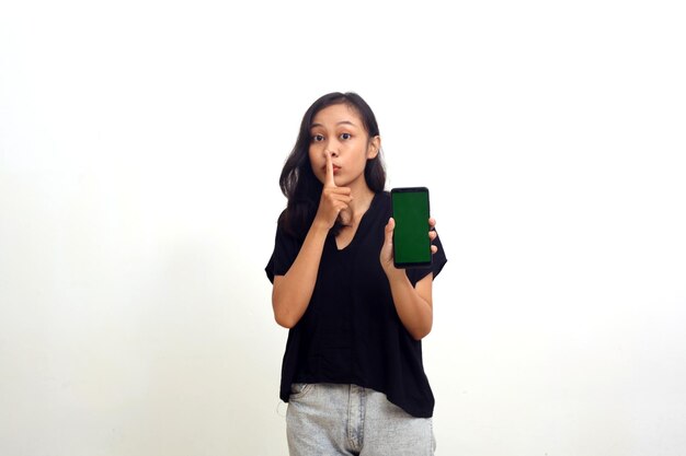 Молодая азиатка показывает секретный жест пальцем, показывая пустой экран, изолированный на белом Premium Фотографии