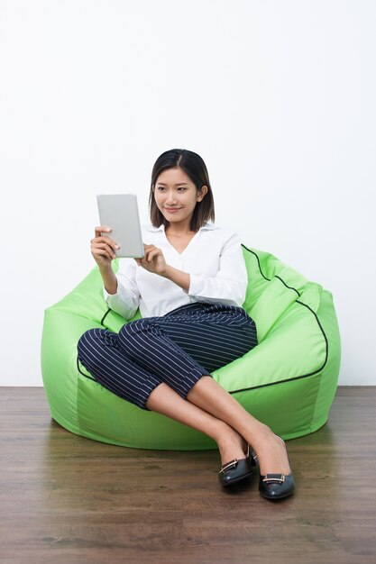 터치 패드를 사용하여 beanbag에 앉아 젊은 아시아 여성
