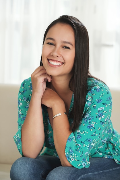 Free photo young asian woman sitting on couch at home and smiling for camera