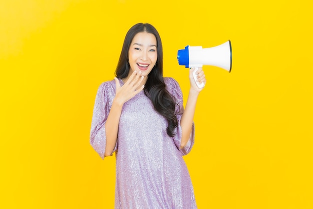 молодая азиатская женщина улыбается с мегафоном на желтом
