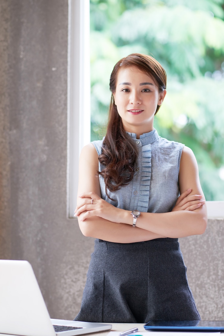 免費 Photo 一位年輕的亞洲女人站在辦公室的辦公桌後面,雙手交叉