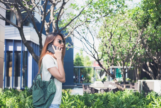 Young Asian woman talking on the smartphone in the garden on weekend. Young woman using smartphone f