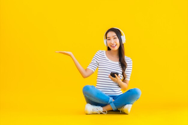 若いアジアの女性は、ヘッドフォンでスマートな携帯電話を使用します。